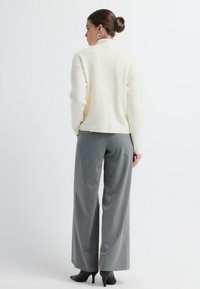 Kremowy sweter z golfem, zestawiony z szarymi, kratkowymi spodniami w szerokiej nogawce, podkreślającymi miękką fakturę i dopasowany krój. Czarne szpilki dopełniają całość.