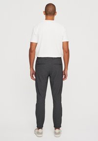 Camiseta blanca de manga corta para hombre combinada con pantalones oscuros grises a medida, con un corte elegante y un sutil detalle de bolsillo en la parte posterior.