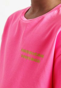 Różowy bawełniany t-shirt z okrągłym dekoltem, krótkimi rękawami oraz złotym napisem „AMERICAN VINTAGE” nadrukowanym z przodu. Gładka tekstura.