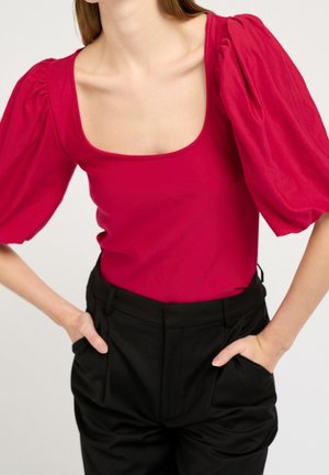 Body ajustado rojo con escote cuadrado y mangas abullonadas, combinado con pantalones negros de tiro alto que tienen bolsillos laterales y una textura suave.