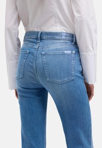 Jasnoniebieskie dżinsy z denimu o dopasowanym kroju, średnim stanie, dwoma tylnymi kieszeniami oraz subtelnym przeszyciem na pasku.