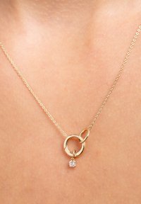 Delicate gold chain necklace with two interlinked gold rings and a small dangling clear gemstone pendant on bare skin.