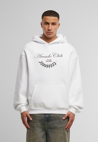 Hoodie bianco con la scritta "Arcade Club" e "Virtual Domain" stampata in nero, caratterizzato da un design a foglia e una tasca a marsupio frontale. Vestibilità casual.