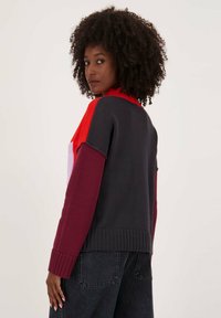 Multikleurige trui met een hoge hals, geribbelde mouwen en zoom. Het materiaal is zacht gebreid en heeft tinten van rood, marineblauw en bordeaux.