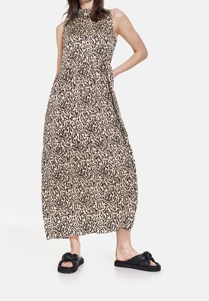 Vestido maxi de tela beige con patrón de manchas negras, diseño sin mangas, cintura ceñida y silueta fluida, combinado con sandalias negras.