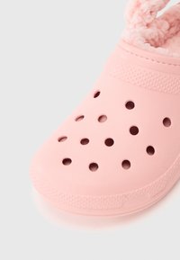 Rosa träskor av klipptyp med ventilationshål och mjukt, fluffigt innerfoder, visade mot en enkel ljus bakgrund.