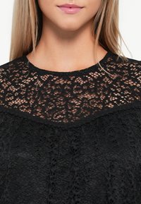 Musta pitsitoppi, jossa on monimutkaisia kukkakuoseja, pyöreä pääntie ja teksturoitu paita, jossa on koottu muotoilu.