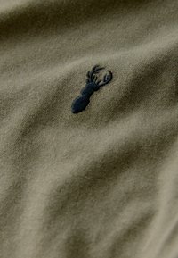 Olivgrön tyg har en strukturerad yta med en mörkblå broderad hummerdesign som är placerad off-center.