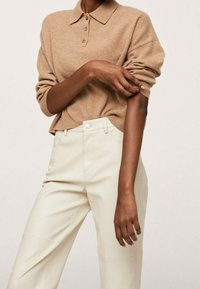 Osoba ubrana w beżowy sweter polo z długim rękawem, podniesionymi rękawami i spodniami w kolorze off-white o wysokim stanie.
