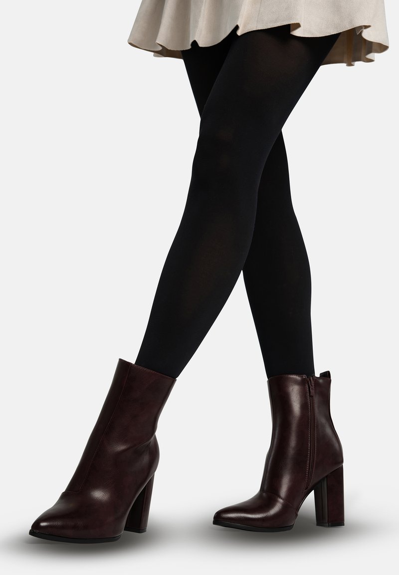 Bordeauxrode enkellaarsjes met hak, een gladde synthetische textuur, een puntige neus en een ritssluiting aan de zijkant. Gecombineerd met zwarte maillots.