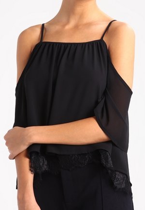 Blusa nera con spalle scoperte, spalline sottili, scollatura arricciata e bordo in pizzo. Realizzata in tessuto leggero e fluido.