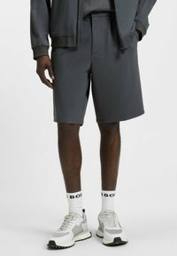 Donkergrijze sportshorts van gladde stof, met een gestructureerde taille en een platte voorkant. Gecombineerd met witte sokken en grijze sneakers.