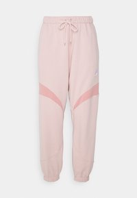 Světlé růžové Nike tepláky s elastickým pasem, šňůrkou, manžetami na kotnících a tmavšími růžovými zakřivenými panelovými akcenty na nohavicích.