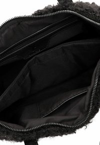 Melnā rokas soma iekšpuse ar divām ievelkamām kabatām un teksturētu, pūkainu oderi. Viens tonis melnas auduma ar gludu virsmu. Redzami rāvējslēdzēju akcenti.