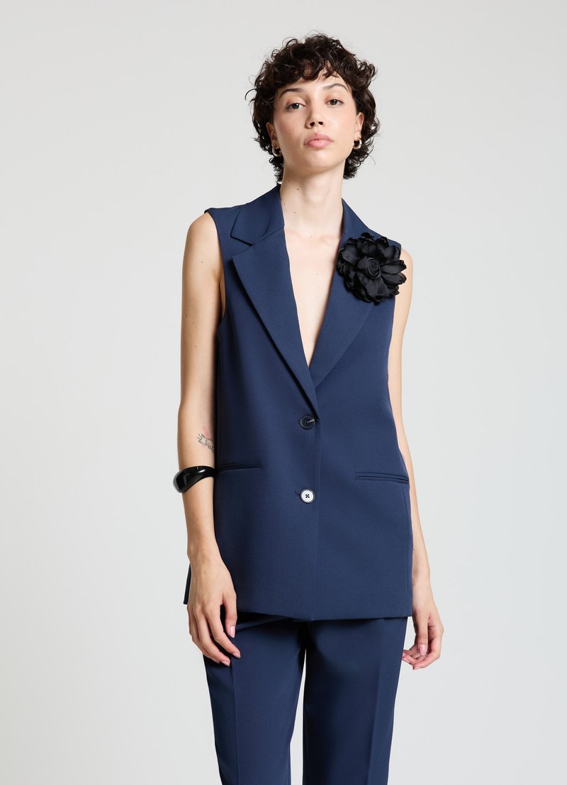 Blazer sans manches bleu marine avec col cranté, fermeture à un bouton, poches avant et accent en fleur de tissu noir sur l'épaule.