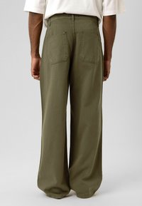 Olijfgroene katoenen broek met wijde pijpen, hoge taille, zichtbare achterzakken en een gladde, gestructureerde afwerking.