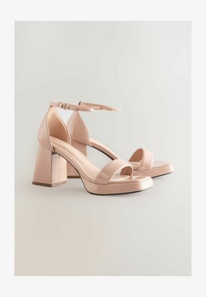 Pirosító rózsaszín magassarkú szandálok masszív, négyzet alakú sarokkal, nyitott orral, bokapánttal és fényes lakkozott felülettel. Sima textúra minimális részletezéssel.
