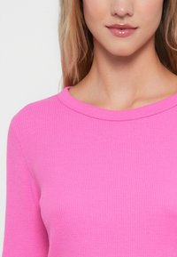 Dopasowany różowy top z prążkowanego dzianiny z okrągłym dekoltem i długimi rękawami, prezentujący gładką teksturę i delikatny stretch.
