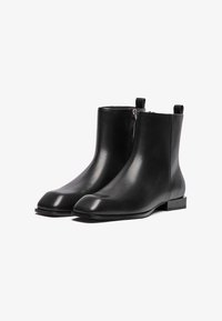Bottines en cuir noir avec une finition lisse, bout arrondi, fermeture éclair sur le côté et petit talon carré. Elles disposent d'anses à l'arrière.
