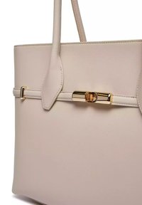 Beige handtas met een gladde lederen textuur, gestructureerde vorm, twee handgrepen en een gouden hardware sluiting detail op een decoratieve riem.