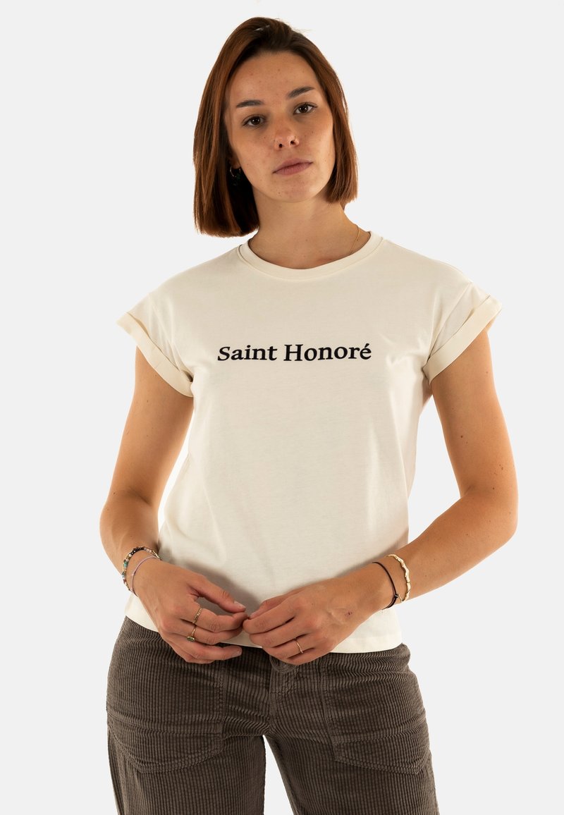 T-shirt in cotone crema con maniche arrotolate, caratterizzato da testo nero "Saint Honoré" posizionato centralmente. Tessuto morbido, vestibilità rilassata.