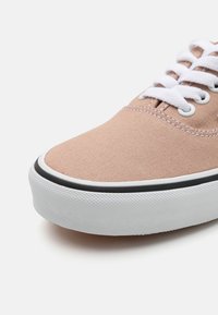 Ljus persika canvas sneakers med vita snören, med en texturerad vit gummisula och svarta detaljer längs kanten. Rundad tådesign.