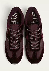 Baskets bordeaux présentant un mélange de matériaux, y compris du velours et un tissu lisse, avec des lacets à motifs et une semelle texturée.