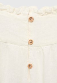 Tissu en lin couleur crème avec un bord supérieur froncé et cinq boutons en bois clair le long du dos, créant un look texturé.