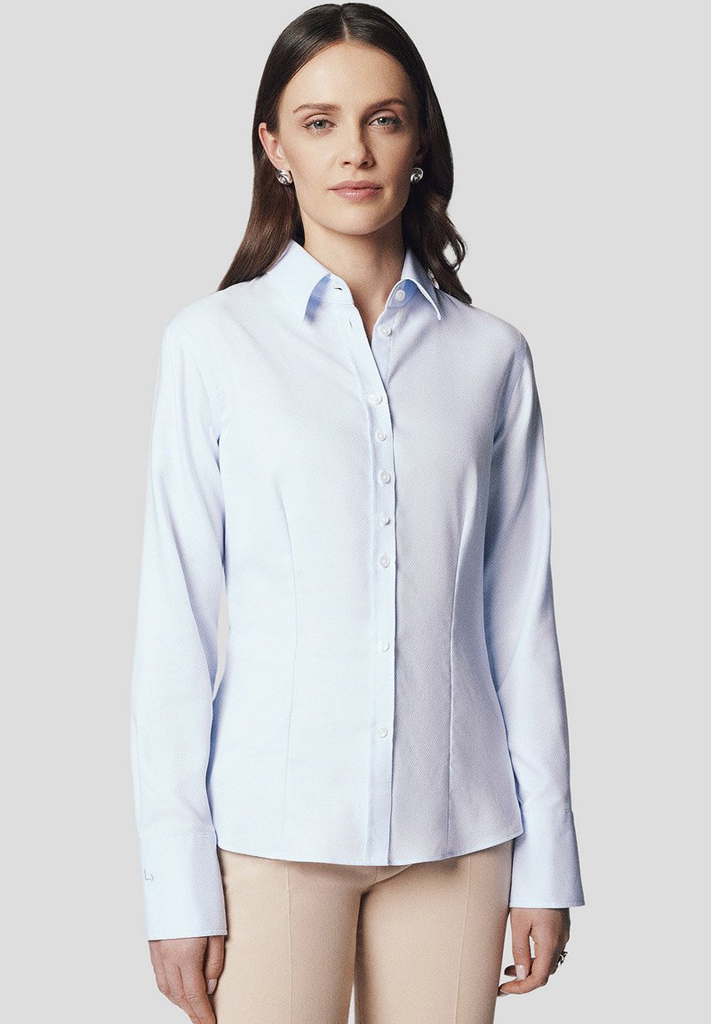 Jasnoniebieska koszula z długim rękawem zapinana na guziki z kołnierzykiem, wykonana z fakturowanej tkaniny, o dopasowanym kroju, w zestawie z beżowymi spodniami.