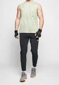Světl zelený, bezrukávový sportovní top s texturovaným vzorem. Černé tréninkové kalhoty a šedé sportovní boty s červenými akcenty. Zahrnuté rukavice.