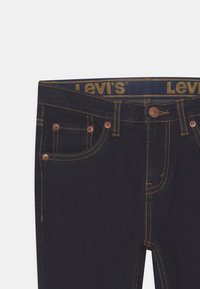 Vaqueros de mezclilla azul oscuro con herrajes de cobre, bolsillos cosidos y una cinturilla con el logo de Levi's. Presentan un diseño tradicional de 5 bolsillos.