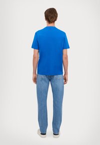 Blue cotton T-shirt with short sleeves, crew neckline, and a straight cut, paired with light blue denim jeans and casual white shoes.