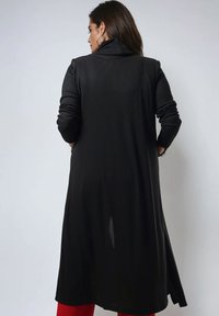 Zwarte lange cardigan met ribbelstructuur, een hoge kraag en lange mouwen, met een flinke zijsplit voor extra beweging en detail.