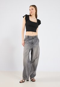 Top negro corto con mangas con volantes, combinado con unos pantalones vaqueros gris de cintura alta y corte suelto, y sandalias de tacón negras. Diseño minimalista.
