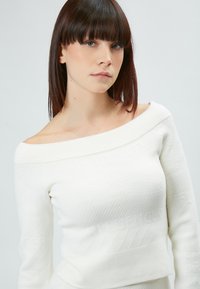 Maglione bianco senza spalle con scollatura a coste, tessuto texturizzato e motivi sottili. Il design aderente mette in risalto la forma del corpo.