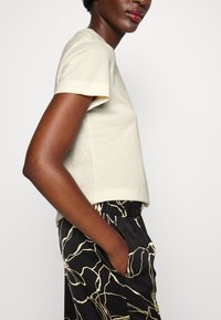 Camiseta de algodón beige claro con mangas cortas, combinada con pantalones negros que presentan un patrón abstracto blanco y una cinturilla elástica.