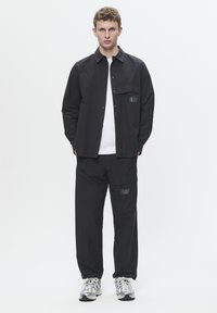 Black button-up shirt with chest pocket, paired with matching black cargo pants featuring a logo. Light-colored athletic shoes with accents.