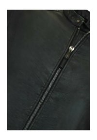 Zwarte leren jack met een gladde textuur, voorzien van een opvallende rits en een staande kraag. De stof heeft een subtiele glans.