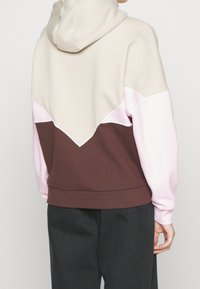 Huvtröja i beige, rosa och brun. Har en färgblockdesign med en diagonal söm och ribbad nederkant. Mjuk tygtextur.