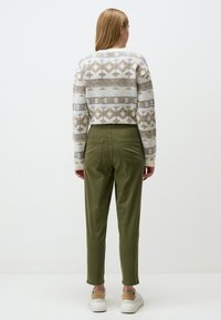 Maglione corto con motivo geometrico in beige chiaro, grigio e marrone, abbinato a pantaloni verde oliva a sigaretta e sneakers bianche.
