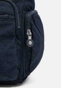 Navy blue fabric bag featuring a prominent zipper and a round logo tag. The texture is smooth with subtle creases and a sturdy design.
