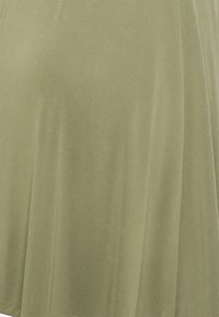 Top verde oliva realizzato in morbido tessuto jersey, con vestibilità ampia, texture liscia e una leggera caduta. Nessun motivo o accessorio visibile.