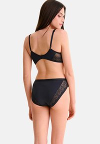 Ensemble de lingerie noire comprenant un soutien-gorge avec bretelles ajustables et détails en dentelle, accompagné d'une culotte taille haute assortie avec accents en dentelle.