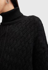 Pull à col roulé en maille noire avec un motif texturé, doté d'un col haut et d'une coupe ample. La laine douce et épaisse est visible en gros plan.