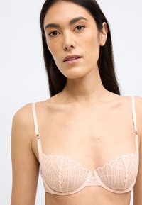 Világos rózsaszín melltartó csipkés díszítéssel, geometriai mintákkal és állítható pántokkal. Puha anyag és merevítő a tartásért.