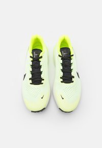 Un paio di scarpe da corsa Nike giallo neon e nere con lacci neri, lati perforati e suole bianche, viste dall'alto su uno sfondo bianco.