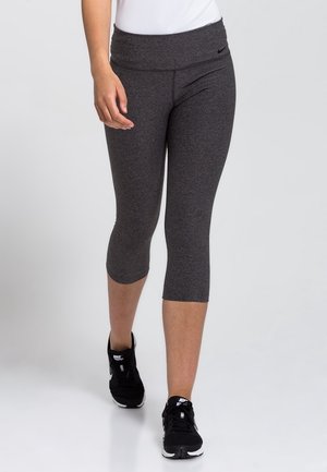 Person iført mørkegrå korte leggings og sorte Nike-sneakers, der går fremad på en ensartet lys baggrund.