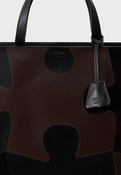 Sac fourre-tout en cuir marron et noir Moschino Milano avec poignées supérieures et une petite étiquette en cuir suspendue à une poignée.