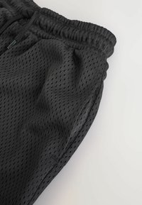 Shorts en maille noire avec un tissu léger et respirant, surface texturée, taille élastique et détails de poches latérales.