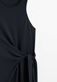 Robe noire sans manches avec un col rond et un détail de lien en tissu froncé à la taille sur fond blanc.